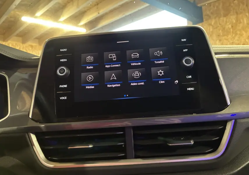 Écran tactile central du Volkswagen T-Roc 2023 affichant le menu principal avec options radio, navigation et aides à la conduite.
