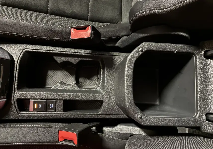 Vue plongeante sur la console centrale noire du Volkswagen T-Roc 2023, avec porte-gobelets et bouton frein à main électronique.