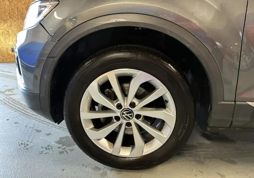 Gros plan sur la roue avant gauche grise d'un Volkswagen T-Roc 2023 avec jante alliage et logo VW central.