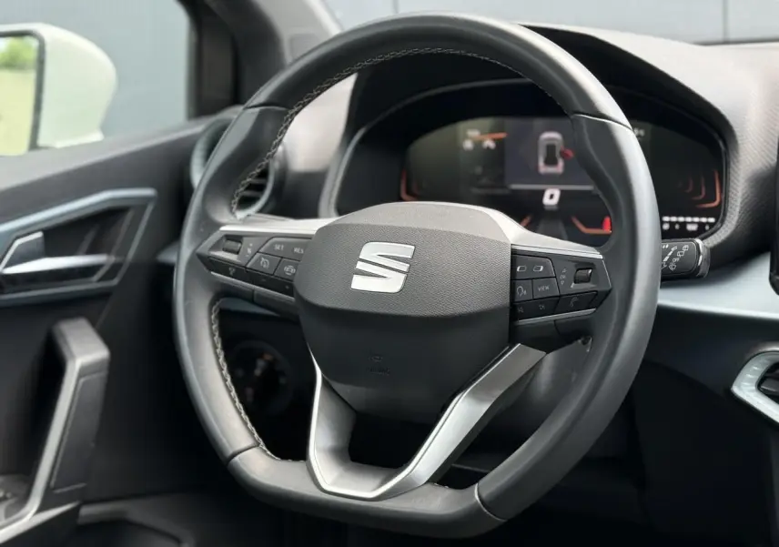 Vue rapprochée du volant noir du SEAT Arona 2025 avec commandes intégrées et tableau de bord digital en arrière-plan.