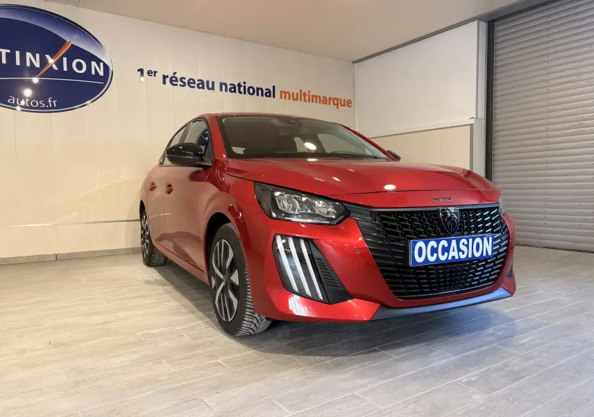 Peugeot 208 rouge vue 3/4 avant droit en intérieur, avec calandre noire et plaque "OCCASION" visible.