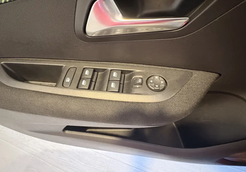 Gros plan sur la commande des vitres électriques et rétroviseurs côté conducteur de la Peugeot 208 Active rouge 2024.