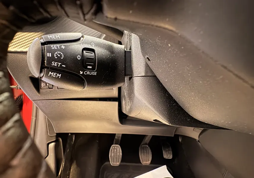 Gros plan sur la commande de régulateur de vitesse à gauche du volant dans l’habitacle d’une Peugeot 208 Active rouge 2024.