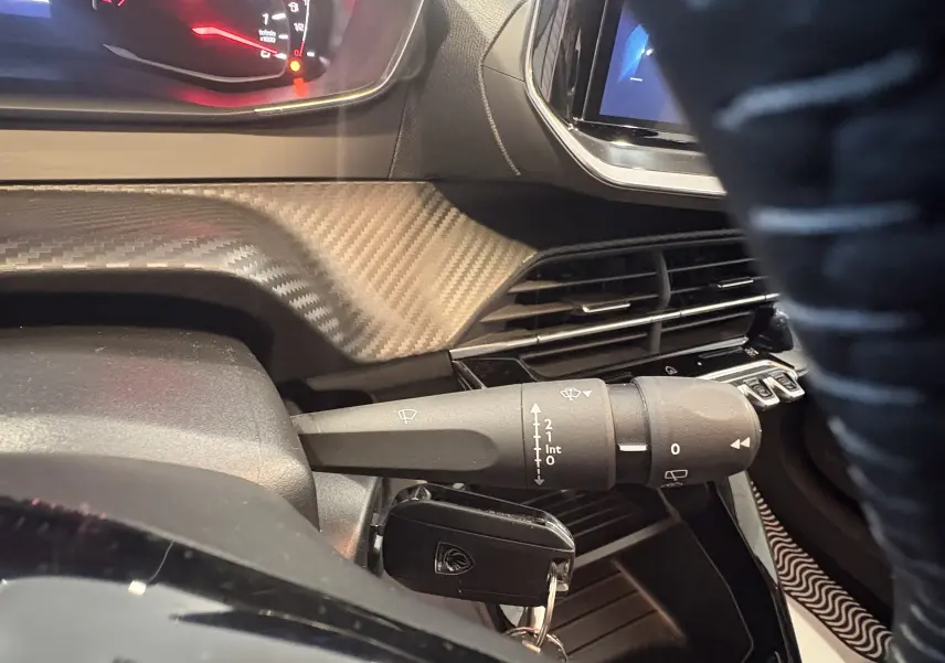 Gros plan intérieur sur la commande d’essuie-glace et le tableau de bord de la Peugeot 208 Active rouge 2024.