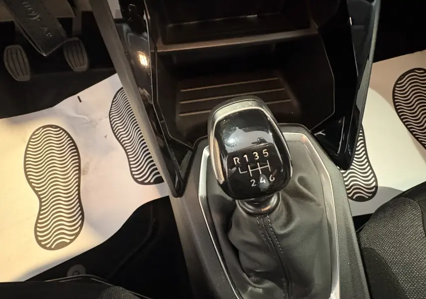 Gros plan sur le levier de vitesses manuel noir de la Peugeot 208 Active 2024, entouré de tapis blancs avec empreintes.