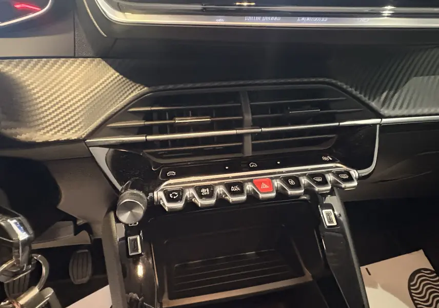 Vue rapprochée du tableau de bord de la Peugeot 208 Active 2024, mettant en valeur les commandes et la finition carbone noire.