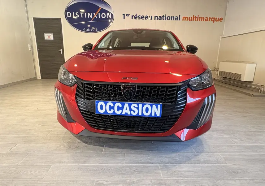 Vue frontale d'une Peugeot 208 Active rouge 2024 avec calandre noire et plaque "OCCASION" en intérieur showroom.