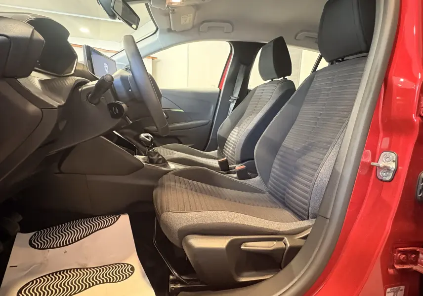 Vue intérieure côté gauche de la Peugeot 208 Active rouge 2024, montrant les sièges tissu noir et la boîte manuelle.