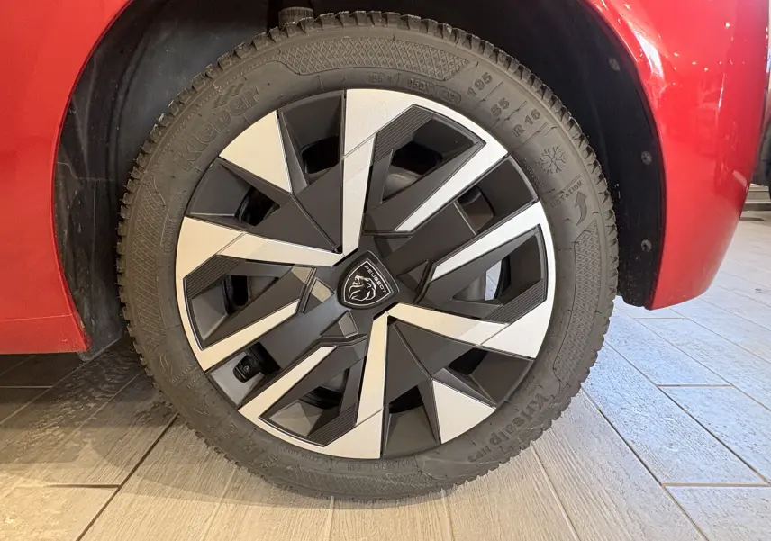 Gros plan sur la roue avant droite d'une Peugeot 208 rouge 2024 avec jante alliage au design géométrique bicolore.