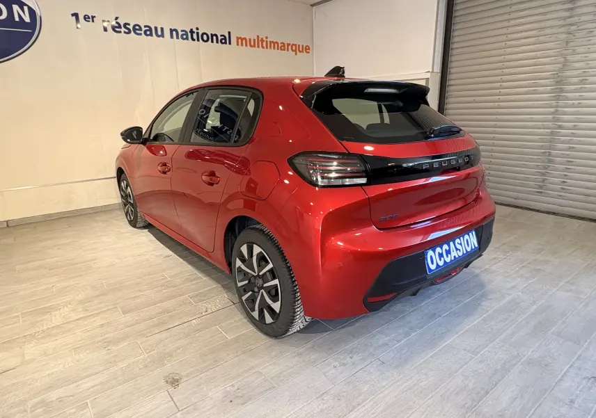 Vue 3/4 arrière droite d'une Peugeot 208 Active rouge 2024 avec feux arrière noirs et jantes alliage bicolores.