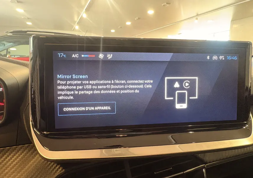 Écran tactile central de la Peugeot 208 rouge 2024 affichant l'interface Mirror Screen en intérieur jour.