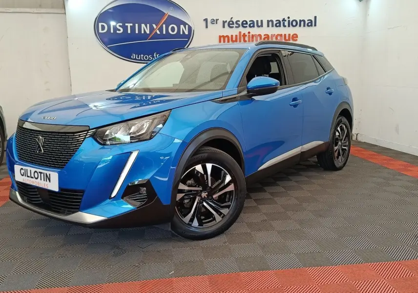 Peugeot 2008 bleu en 3/4 avant droit, avec calandre noire et jantes alliage bicolores visibles en intérieur showroom.