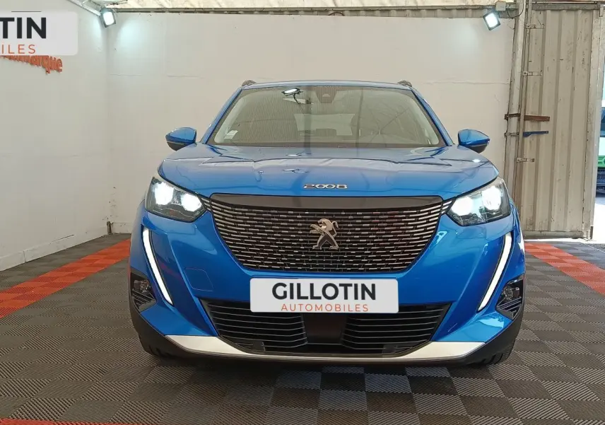 Vue frontale d'un Peugeot 2008 bleu avec calandre noire et feux LED allumés dans un showroom.