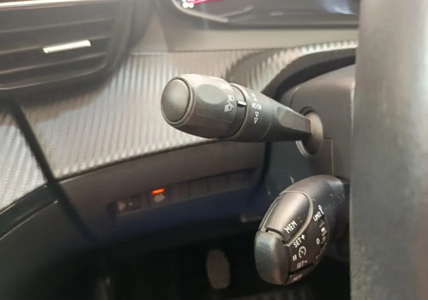 Gros plan sur les commandes de régulateur de vitesse et des phares à gauche du volant d’un Peugeot 2008 bleu 2021.