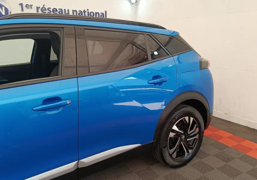 Vue côté droit arrière d’un Peugeot 2008 bleu avec jantes noires et vitres teintées dans un showroom.