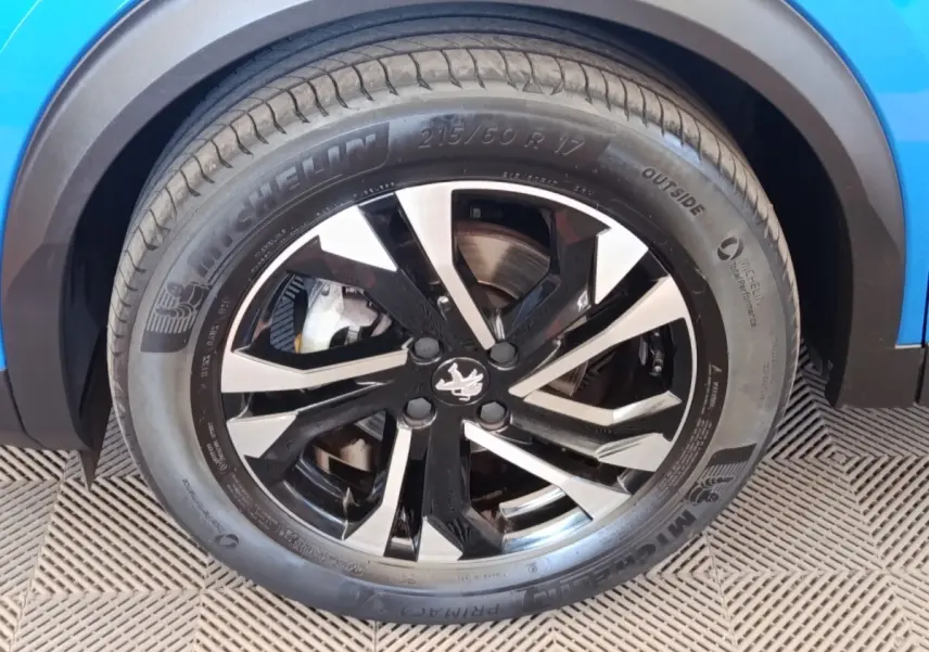 Gros plan sur la roue avant droite d'une Peugeot 2008 bleu, jante alliage noire et argentée avec pneu Michelin.