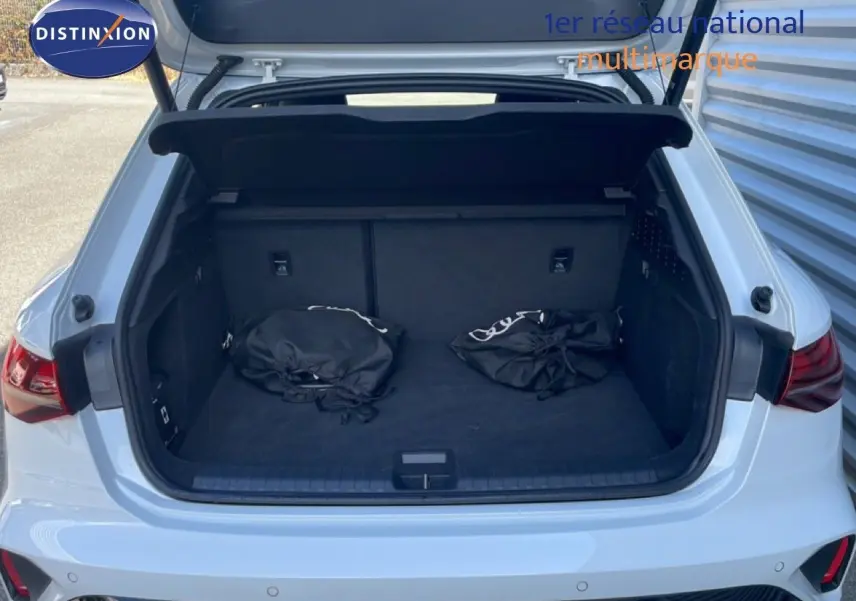 Coffre ouvert vu de l'arrière d'une Audi A3 Sportback blanc ibis avec deux sacs noirs à l'intérieur.