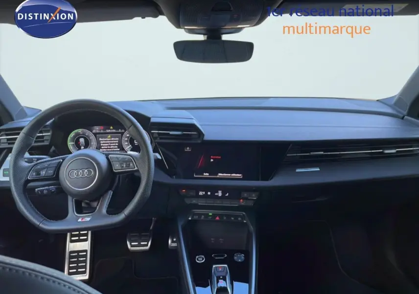 Vue intérieure frontale de l'Audi A3 Sportback 40 TFSIe blanc Ibis, tableau de bord moderne avec écran tactile et volant multifonction.