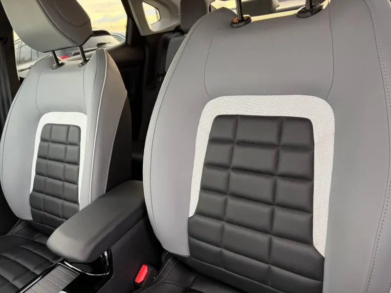 Gros plan sur les sièges avant gris et noir du Citroën C4 X 2025, montrant le détail matelassé et l'accoudoir central.