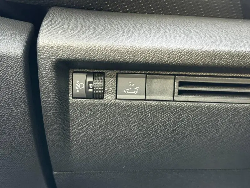 Détail intérieur du tableau de bord côté conducteur du Citroën C4 X 2025, avec commande de réglage des phares et bouton d'ouverture du coffre.