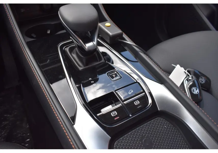 Gros plan sur la console centrale de la MG MOTOR EHS 1.5 Hybrid+ 224 ch Luxury 2026, avec levier de vitesse et clés sur siège gris.