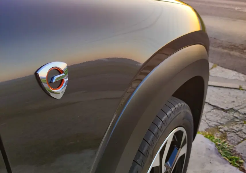 Gros plan sur l'aile avant droite gris foncé du Mazda MX-30 2023 avec logo hybride au coucher du soleil.