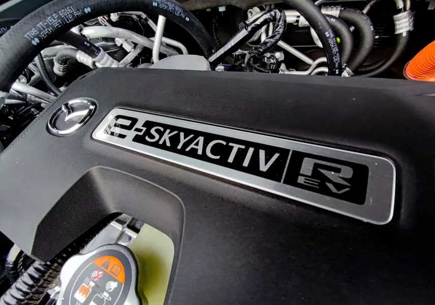 Gros plan sur le moteur e-SKYACTIV d'une Mazda MX-30 2023 hybride rechargeable, avec logo Mazda visible sur la couverture noire.