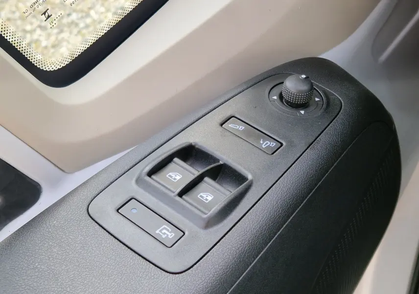 Gros plan sur les commandes de lève-vitres et réglage des rétroviseurs côté conducteur du Citroën Jumper blanc 2023.
