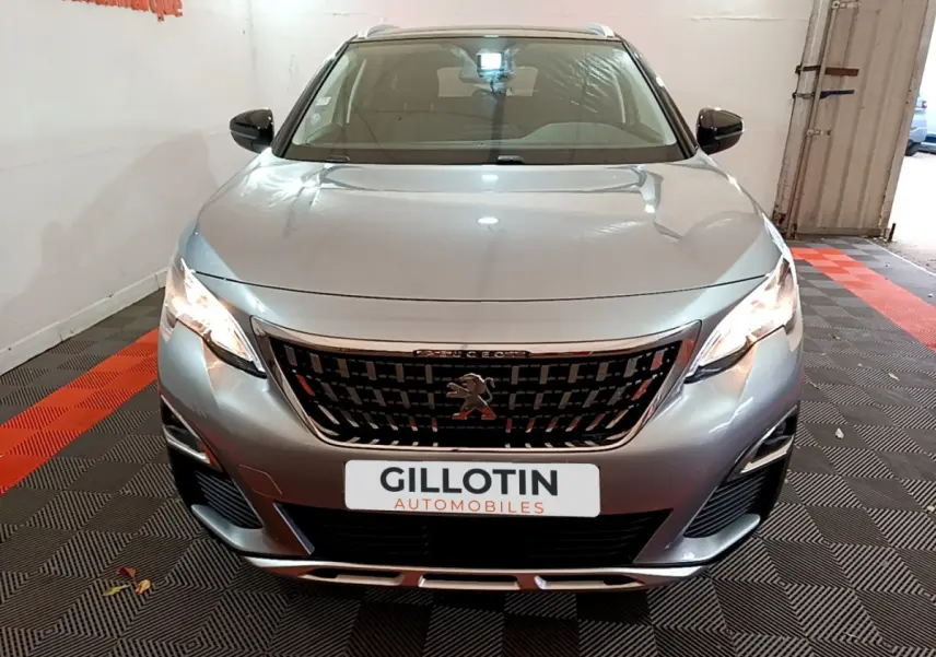 Vue frontale d'un Peugeot 5008 gris clair avec calandre noire et feux LED allumés dans un garage.