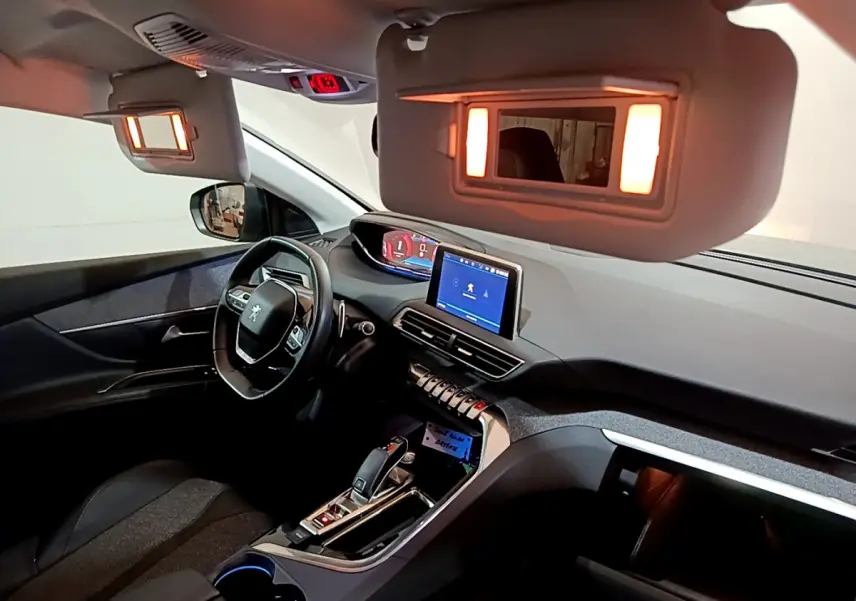 Intérieur du Peugeot 5008 gris clair vu côté conducteur, tableau de bord moderne avec écran tactile et miroir de soleil éclairé.