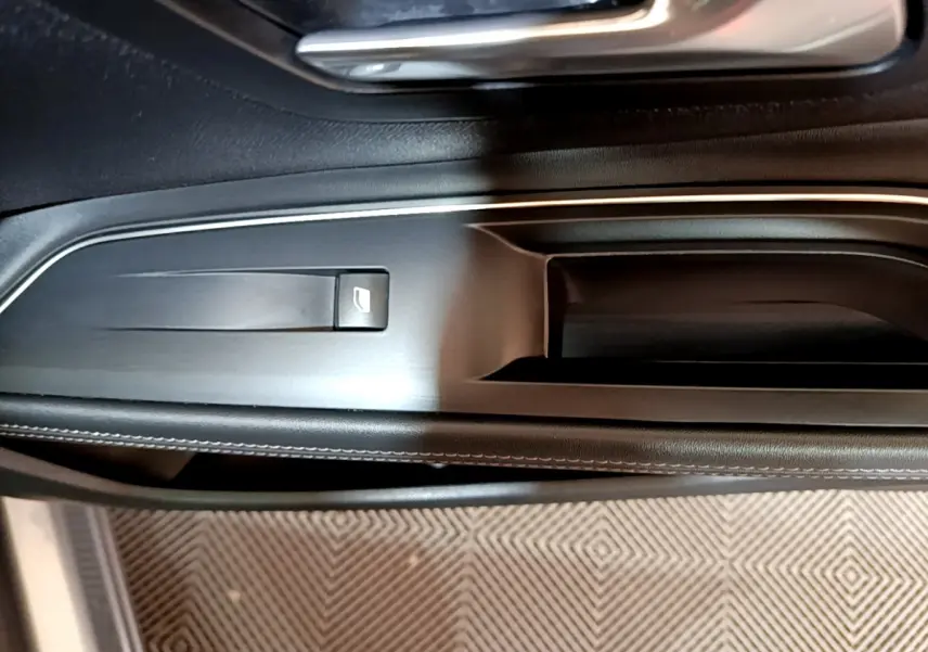 Gros plan sur la poignée intérieure et commande de vitre côté gauche du Peugeot 5008 gris clair, finition Allure.