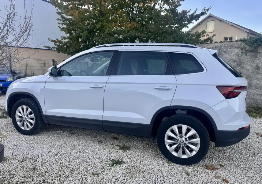 Vue de profil côté gauche d’un Skoda Karoq blanc 2024 garé sur un sol gravillonné avec jantes alliage.