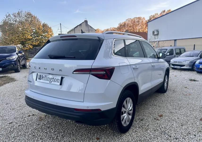 Vue 3/4 arrière droite d’un Skoda Karoq blanc 2024 avec vitres teintées et feux arrière LED distinctifs.