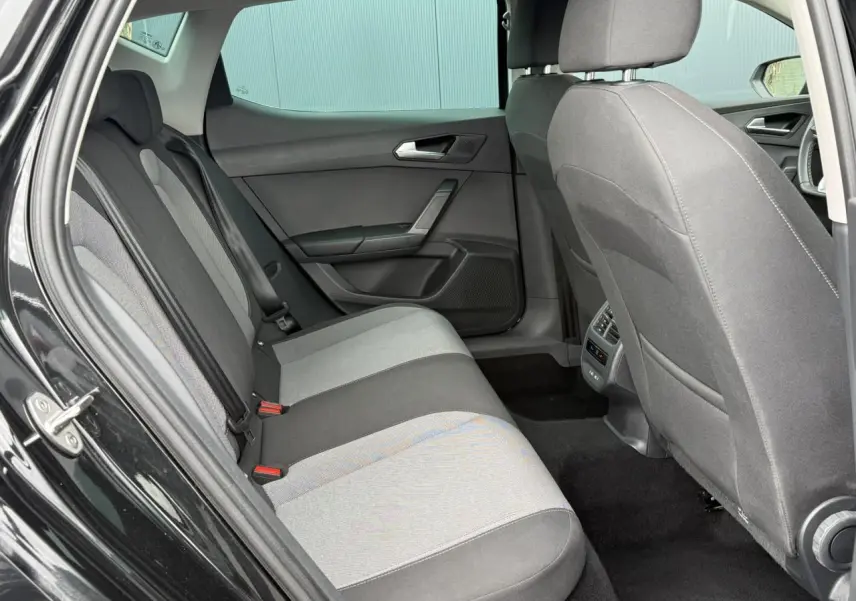 Vue intérieure arrière côté gauche d’une SEAT Leon noir Minuit, montrant les sièges tissu bicolores et les aérateurs arrière.