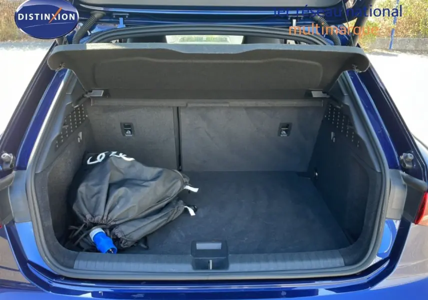 Coffre ouvert vu de l'arrière d'une Audi A3 Sportback bleu Navarre, avec un sac noir et prise de recharge visible.
