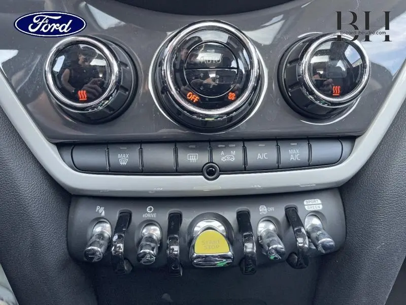 Gros plan sur les commandes centrales du MINI Countryman Cooper SE Moonwalk Grey, avec boutons chromés et bouton Start/Stop jaune.