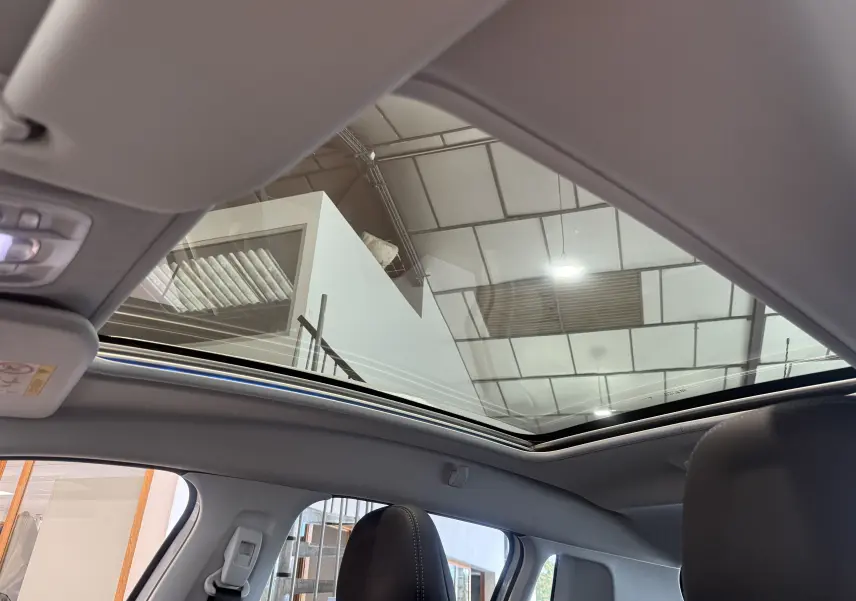 Toit panoramique ouvert vu de l'intérieur du Peugeot 2008 blanc, mettant en valeur les sièges et le plafond clair.