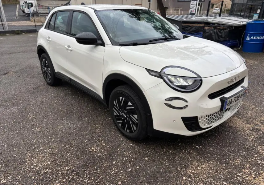 Vue 3/4 avant droit d'une FIAT 600 blanche 2024 avec jantes noires et détails noirs contrastants sur les rétroviseurs et phares.