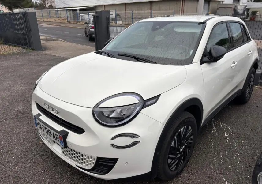 Vue 3/4 avant droite d'une FIAT 600 blanche 2024 avec jantes noires et phares ronds distinctifs.