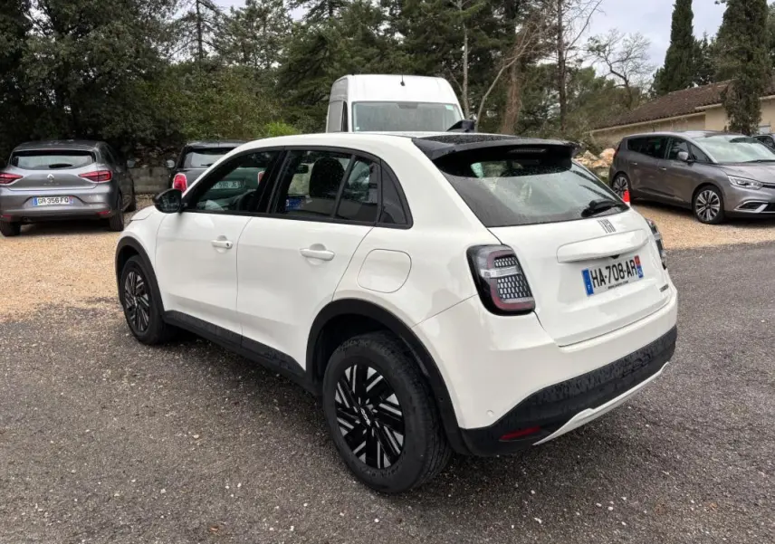 Vue 3/4 arrière droite d'une FIAT 600 blanche 2024 avec toit noir et jantes noires classiques.
