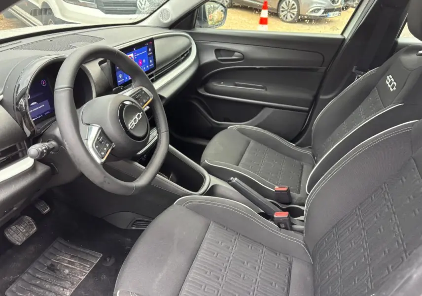 Vue intérieure côté conducteur de la FIAT 600 Hybrid 2024 avec sièges noirs et tableau de bord moderne.
