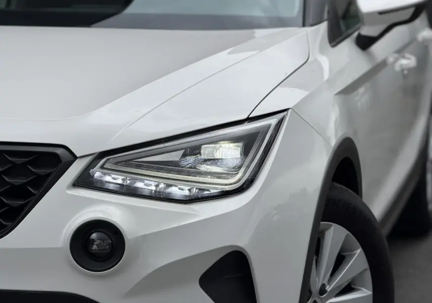Gros plan sur l'avant droit blanc du SEAT Arona 2025, mettant en valeur le phare LED et la calandre noire.