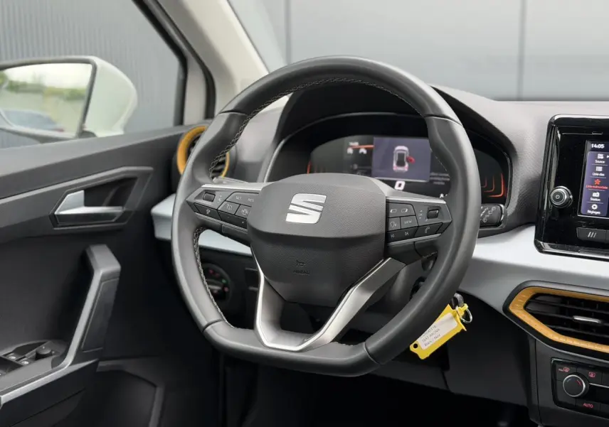 Vue intérieure centrée sur le volant noir du SEAT Arona 2025 avec détails jaunes autour des aérateurs.