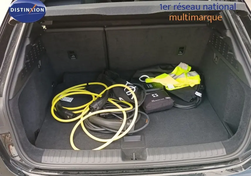 Coffre ouvert vu de l'arrière d'une Audi A3 Sportback noir mito metal avec câbles de recharge et gilet jaune.