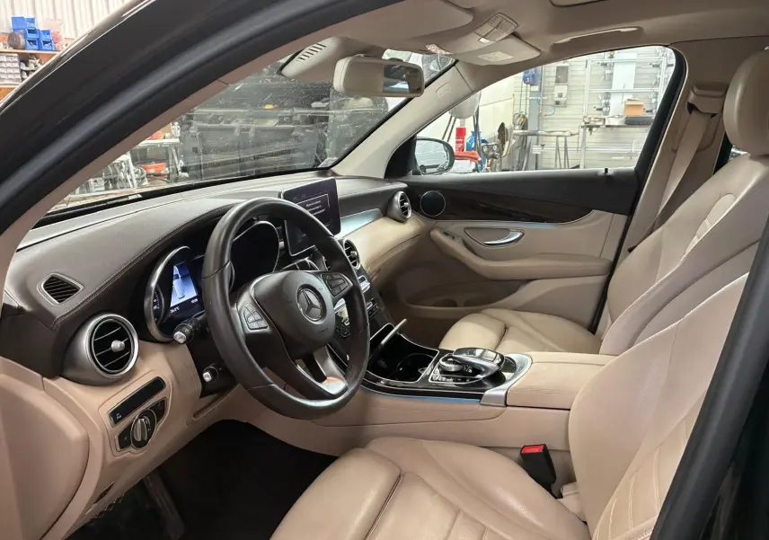 Vue intérieure côté conducteur d’un Mercedes GLC 220D Fascination 2017 avec sellerie cuir beige et tableau de bord noir.