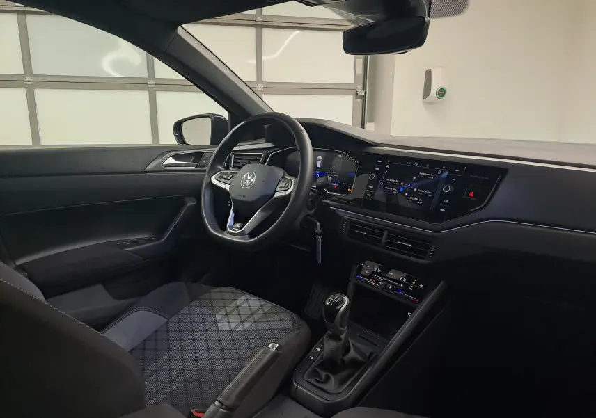 Vue intérieure côté conducteur de la Volkswagen Polo 2025, tableau de bord moderne et siège à motif écossais gris.