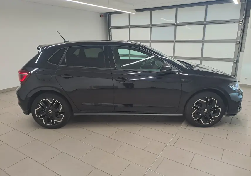 Vue de profil côté gauche d'une Volkswagen Polo 2025 noire intense avec jantes R-Line distinctives en intérieur lumineux.