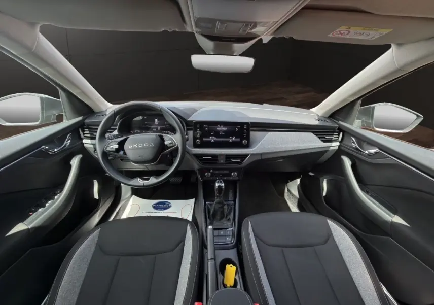 Vue intérieure avant de la Skoda Scala 2025, montrant tableau de bord gris clair et sièges bi-ton noir et gris.