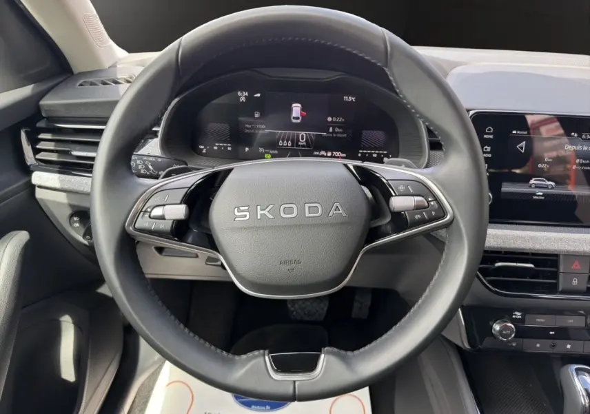 Vue intérieure centrée sur le volant cuir noir SKODA avec tableau de bord numérique et écran tactile gris foncé.