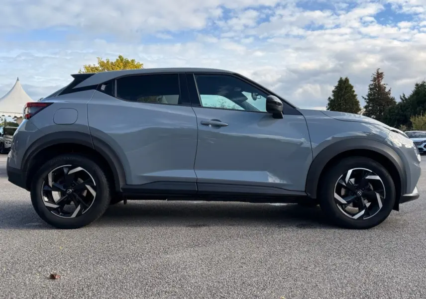 Nissan Juke gris clair vue de profil côté gauche, avec jantes noires et vitres teintées.